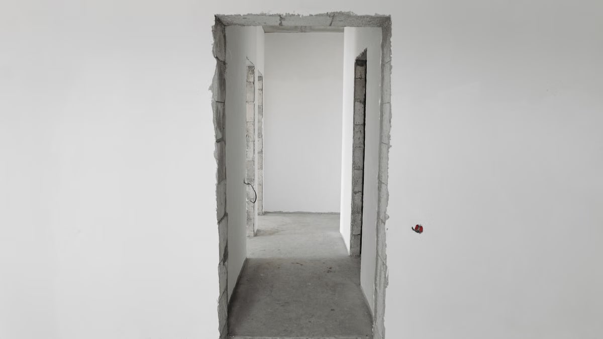 Interior view of a simple white corridor in an unfinished building, showing raw construction details.